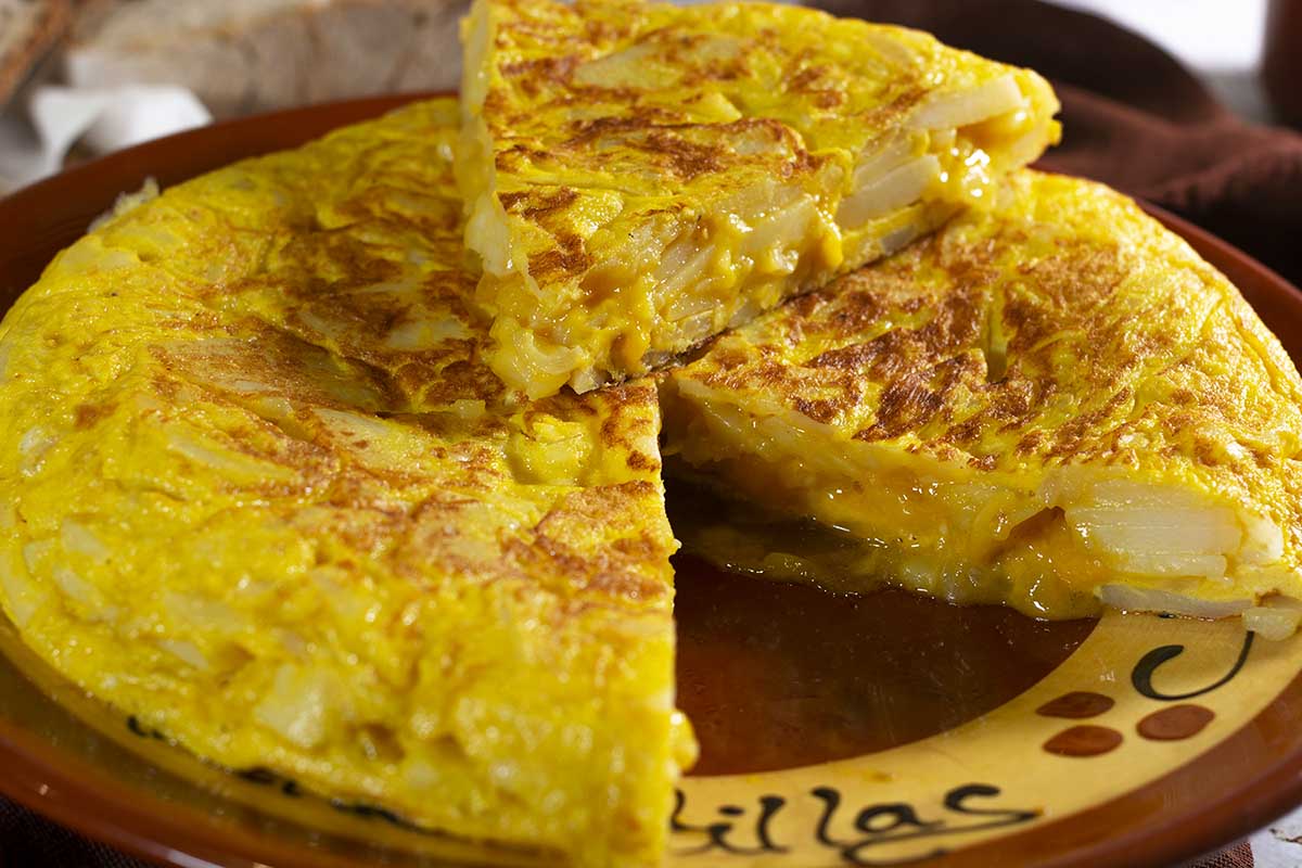 Tortilla de patatas cortada en triangulos, permitiendo ver la patata y el huevo poco hecho en la tortilla